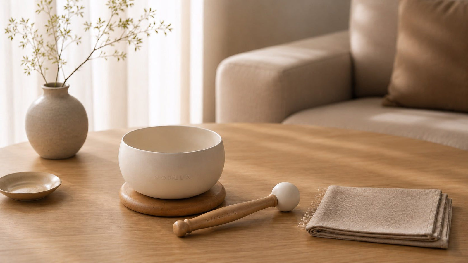 NORLUA Warm Ivory singing bowl with wooden mallet and soft care cloth in a modern home