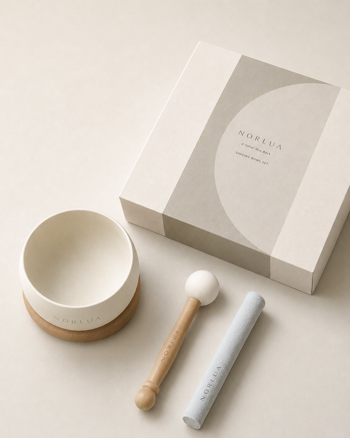 Angled flat lay of the NORLUA singing bowl set with gift box, wooden base, playing stick, and mallet