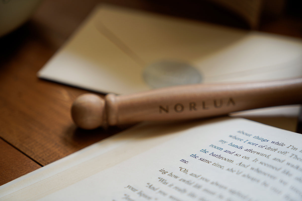 NORLUA Wooden mallet beside an open book and branded envelope on a wooden table.
